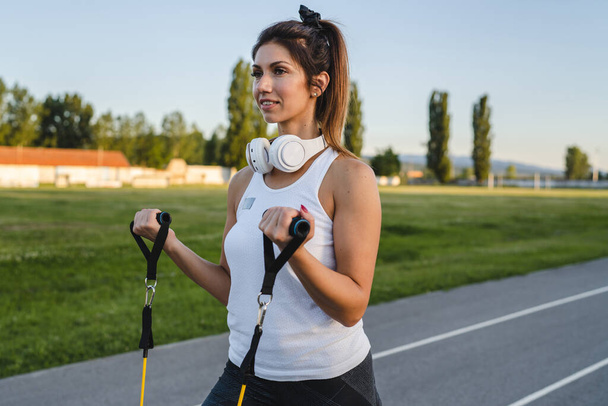 One woman adult caucasian female athlete training with elastic rubber resistance bands in stadium on track in summer evening or morning happy brunette health and fitness concept copy space - Fotoğraf, Görsel