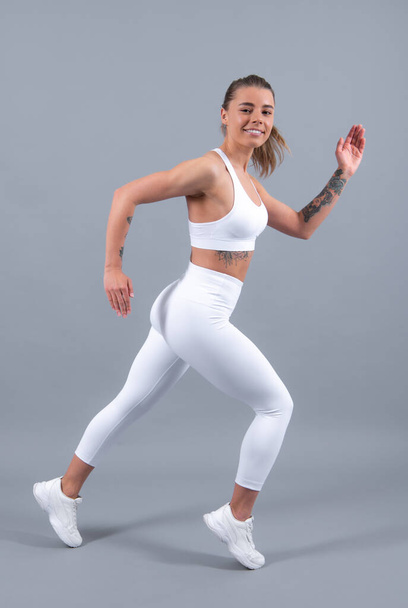 Workout sport motivation concept. Young fitness woman runner stretching legs before run. Sporty woman runner on gray background. Dynamic movement. Sport and healthy lifestyle - Foto, immagini