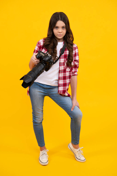 Full length of teen girl with dslr professional photo camera with big photo lens. Kid photographer isoalted on yellow background. Photo school - Zdjęcie, obraz