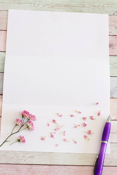 Blanco witte A4page met bloemen en pen op houten tafel - Foto, afbeelding