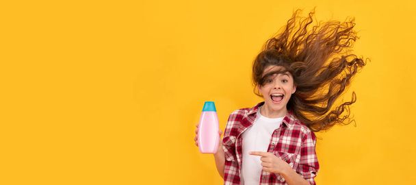 happy teen girl with long curly hair hold shampoo bottle, beauty. Banner of child girl hair care, studio poster header with copy space - Foto, Imagen