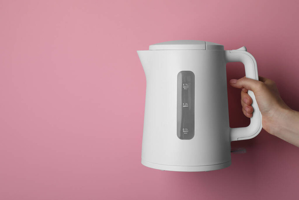Woman holding modern electric kettle on pink background, closeup. Space for text - Φωτογραφία, εικόνα
