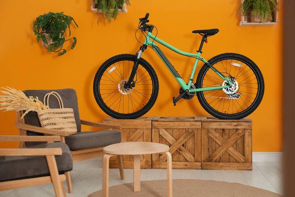 Modern bicycle near orange wall and comfortable armchairs in stylish living room interior - Фото, зображення