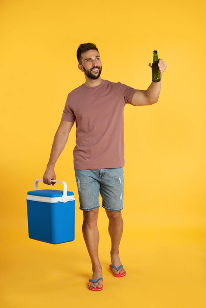 Happy man with cool box and bottle of beer on yellow background - Fotografie, Obrázek