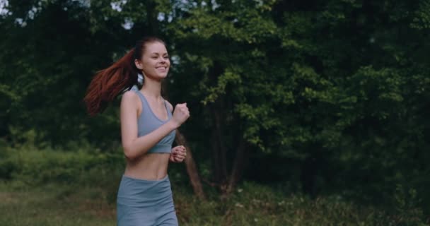 Vrouw op een ochtend joggen in het park in een trainingspak tegen een achtergrond van bomen. Hoge kwaliteit 4k beeldmateriaal - Video