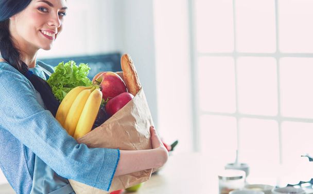 Jovem mulher segurando supermercado saco de compras com legumes .Standing na cozinha. - Foto, Imagem