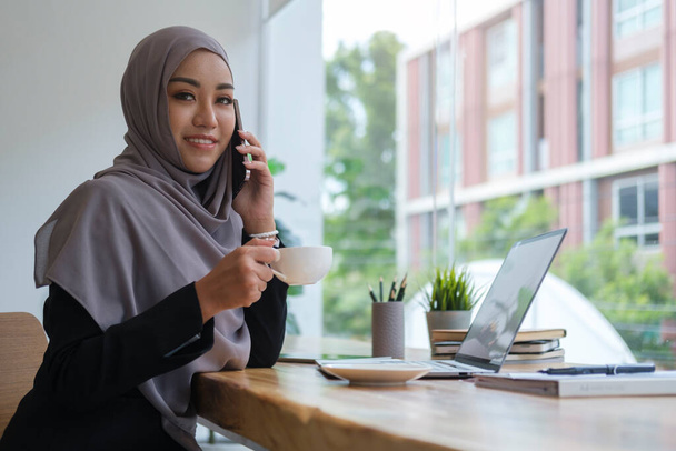 Красива мусульманська бізнес-леді п'є каву і розмовляє по мобільному телефону зі своїм діловим партнером
. - Фото, зображення