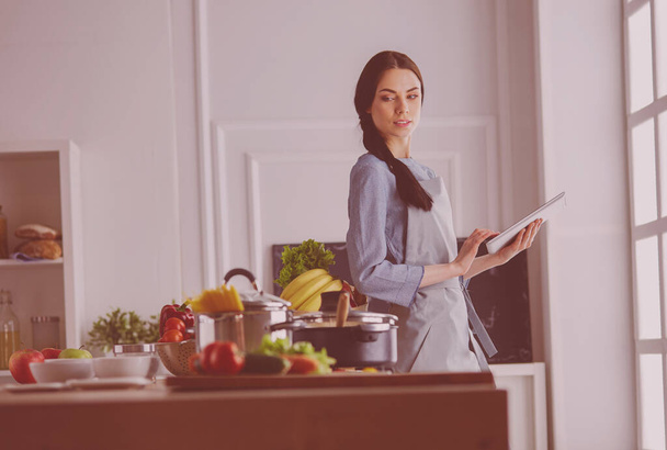 Young woman using a tablet computer to cook in her kitchen. - Foto, Bild