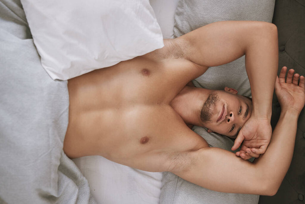 Im ready for the day. High angle portrait of a handsome and muscular young man lying in his bed at home - Foto, Imagem