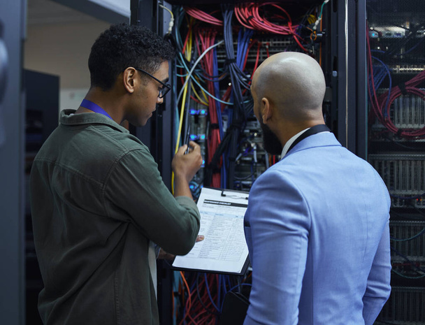 Explaining the ins and outs. two male IT support agents working together in a dark network server room - Foto, Imagen