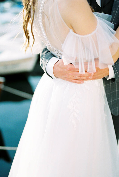 Hands of groom in a plaid jacket hug the waist of bride in a white dress. High quality photo - 写真・画像