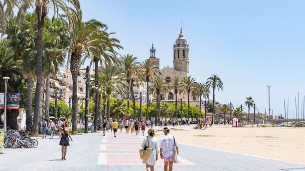 Sitges, Spain - June 12, 2022: Sitges seafront promenade with the background of the church of Sant Bartomeu and Santa Tecla in Sitges (Spain). - Zdjęcie, obraz