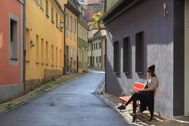Teenage girl sitting on the bench on old city street - Фото, изображение