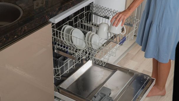 Домогосподарка бере чисті чашки з посудомийної машини
 - Фото, зображення