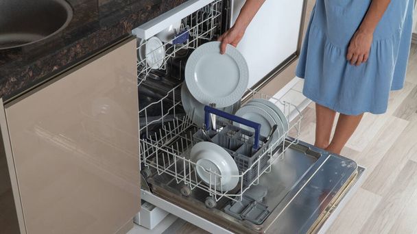Žena v domácnosti vytáhne čisté talíře z myčky nádobí zblízka - Fotografie, Obrázek