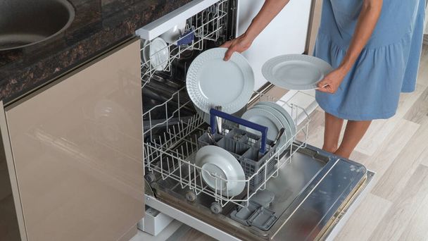Žena v domácnosti vytáhne čisté talíře z myčky nádobí zblízka - Fotografie, Obrázek