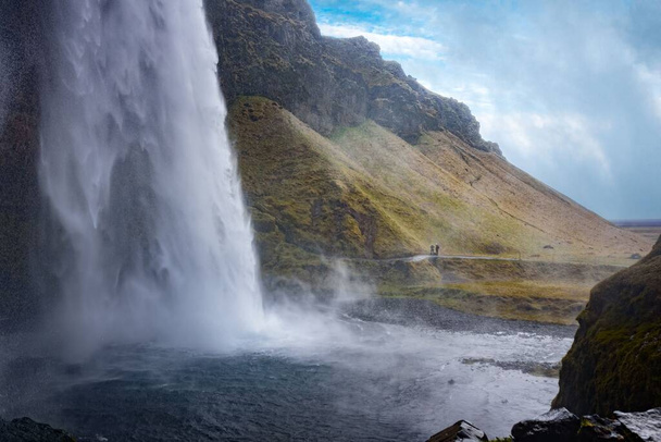 A mesmerizing view of the huge Skogafoss waterfall with tourists  in Iceland - Zdjęcie, obraz