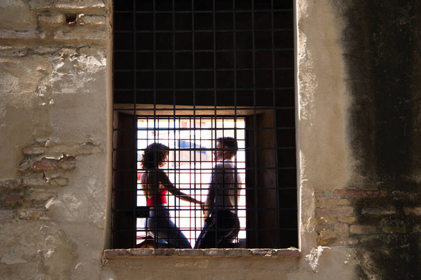 Couple are climbing on a window of an abandoned building. The couple can be seen through the bars. - Photo, image