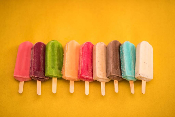 A Top view of colorful ice cream bars in row on the yellow background, giving summer vibes - Foto, Bild