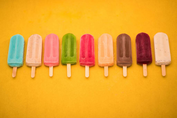 A Top view of colorful ice cream bars in row on the yellow background, giving summer vibes - Foto, Bild