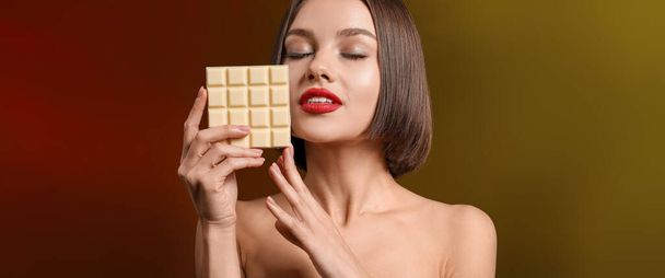Beautiful woman with sweet white chocolate on dark color background   - Фото, изображение