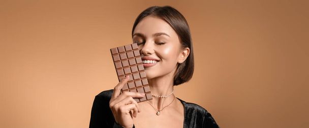 Mooie vrouw met zoete chocolade op bruine achtergrond  - Foto, afbeelding
