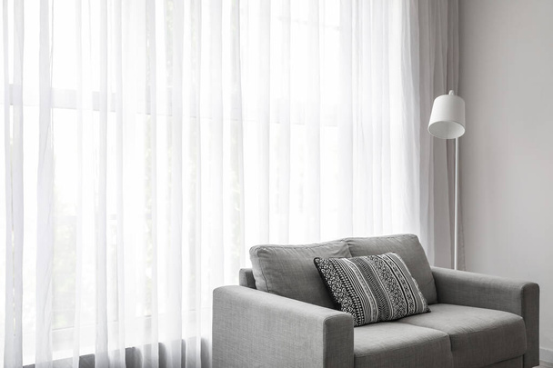 Interior of light living room with grey sofa, standard lamp and curtain - Φωτογραφία, εικόνα