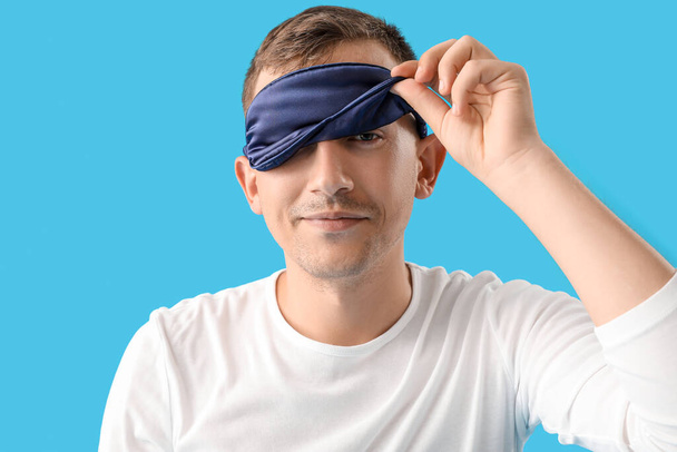 Young man with sleeping mask on blue background - Photo, Image