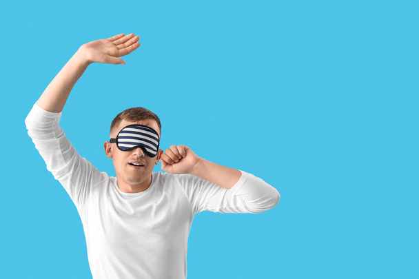 Young man with sleeping mask stretching on blue background - Foto, Bild