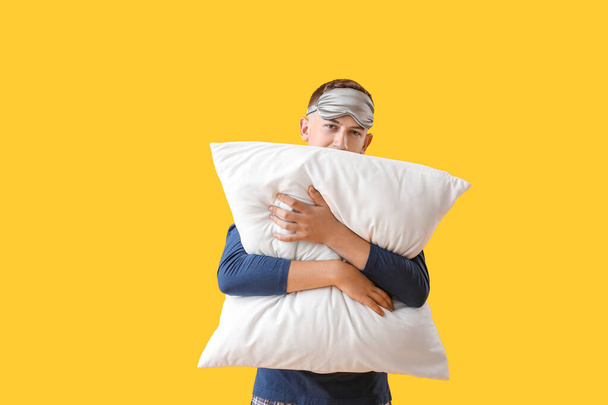 Young man with sleeping mask hugging pillow on yellow background - Photo, image
