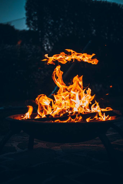 A vertical shot of a bonfire burning in a metallic bowl on a sandy beach at night - Φωτογραφία, εικόνα