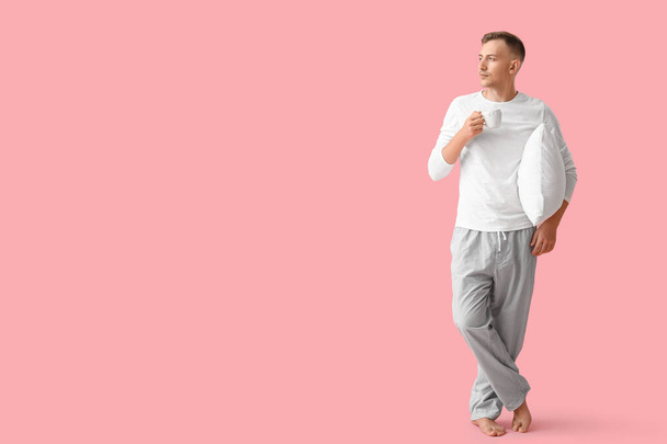 Young man with cup of coffee and pillow on pink background - Fotografie, Obrázek
