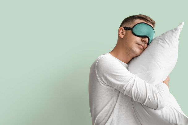 Young man with sleeping mask and pillow on green background - Photo, Image