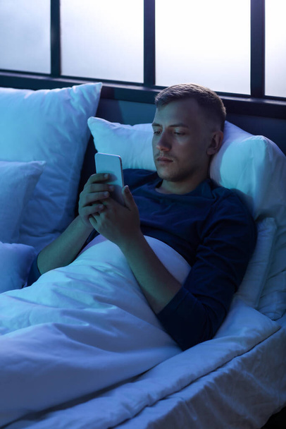 Young man using mobile phone in bedroom at night - 写真・画像