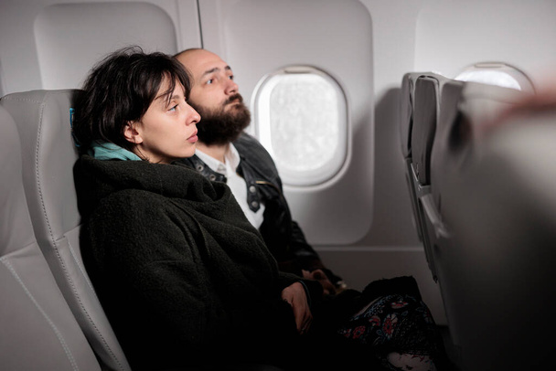 Caucasian travellers having conversation on commercial flight, travelling by plane to go on holiday journey destination. Couple flying abroad with airplane transport to arrive on vacation. - 写真・画像
