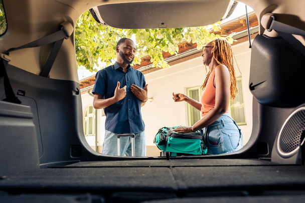Afrika kökenli Amerikalı çift, seyahat çantalarını ve tramvayı bagaja koyup tatil için otomobille ayrılmaya hazırlanıyorlar. Bavullar ve bavullarla araba yolculuğu.. - Fotoğraf, Görsel
