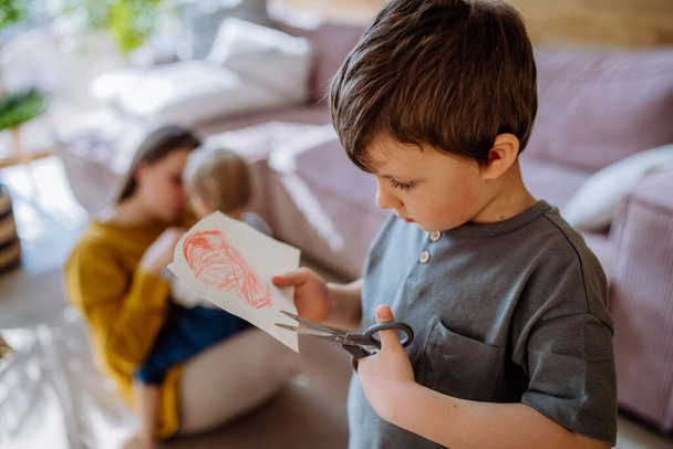 A little boy cutting drawn picture, having creative time in home. - Fotó, kép