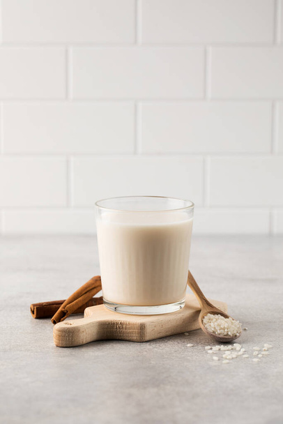 Cold drink based on Horchata rice in a glass on a wooden board with cinnamon sticks on a light background.Vegetarian soft drink, national cuisine. - Foto, Imagen