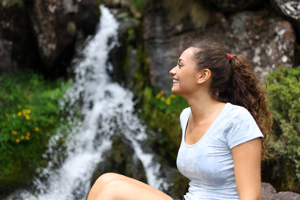 Happy woman contemplating waterfall in a creek in the mountain - Фото, изображение