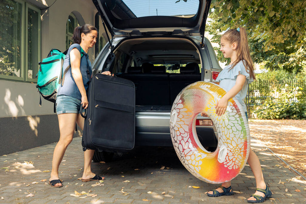Mother and little girl leaving on vacation, loading luggage, bags and inflatable in trunk of automobile to travel at seaside. Family travelling on holiday journey with car during summer. - Foto, immagini