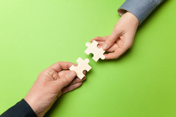 Two hands connect puzzles on a green background. Cooperation and teamwork in business. Collaboration people for success. - Photo, Image