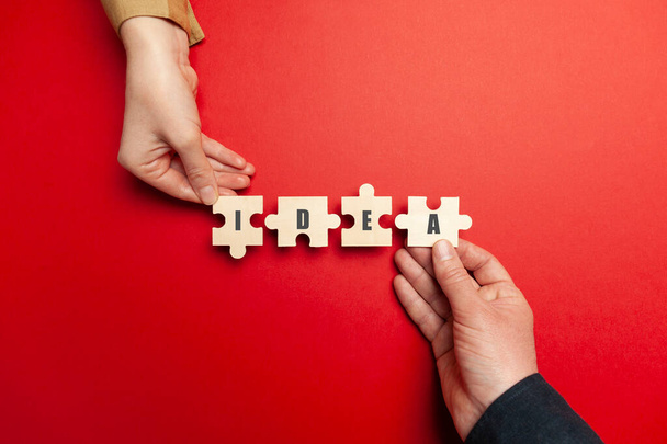 Hands of businessmen folded the word "IDEA" from puzzles on red background. Creative strategy and business solution. Brainstorming for innovations. - Foto, Imagen