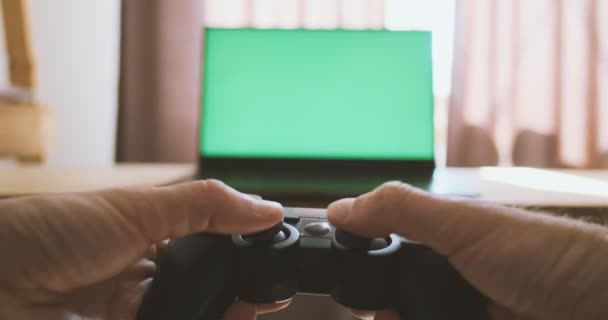 Gamepad a kezében, játszik konzol a háttérben a zöld monitor. Férfi kéz tartsa játék joystick és nyomja meg a gombokat, mozgassa a botokat. Kiváló minőségű 4k felvételek - Felvétel, videó