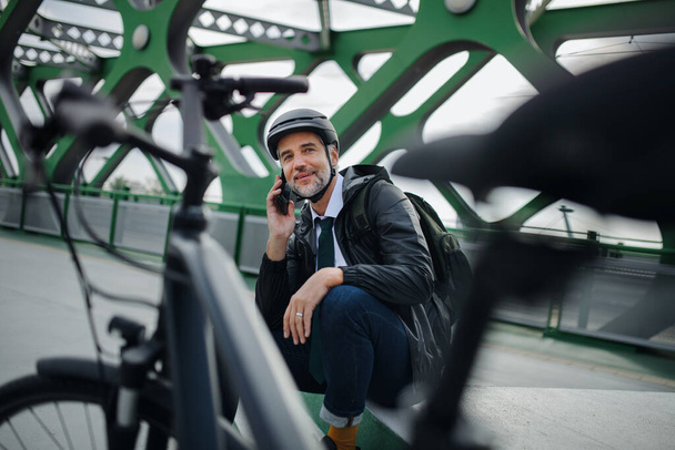 A businessman with bike sitting on bench, using smartphone. Commuting and alternative transport concept - Foto, Imagem
