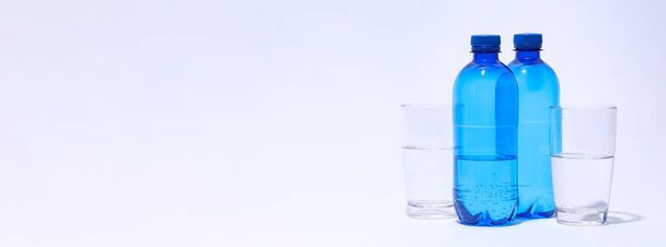 Blue plastic bottles and glasses of water on light background - Foto, afbeelding
