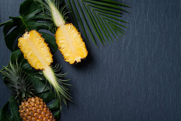 Top view of fresh cut pineapple with tropical leaves on dark blue background. - Φωτογραφία, εικόνα