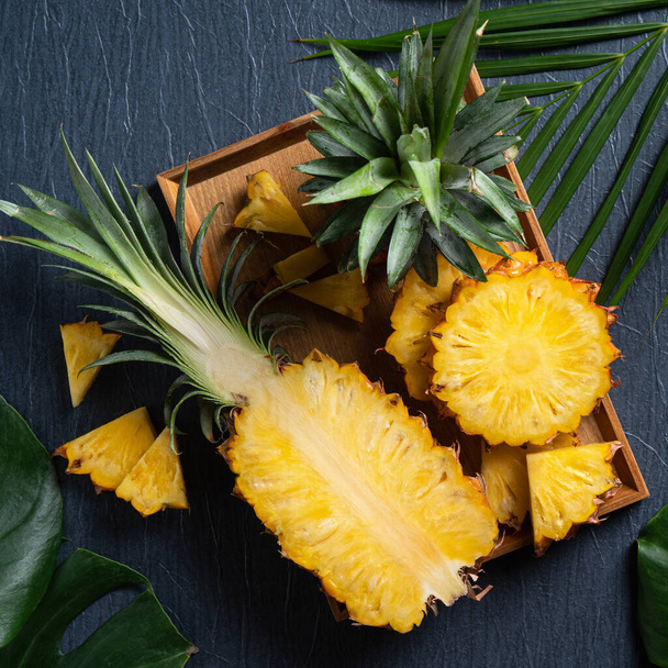 Vue de dessus de l'ananas frais coupé avec des feuilles tropicales sur fond bleu foncé. - Photo, image