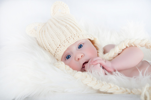 Un joli petit bébé regarde dans la caméra et porte un chapeau blanc. Le bébé pourrait être un garçon ou une fille et a les yeux bleus
. - Photo, image