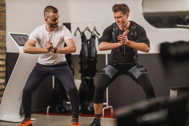 Mann mittleren Alters macht EMS-Training mit Personal Trainer im Fitnessstudio. - Foto, Bild