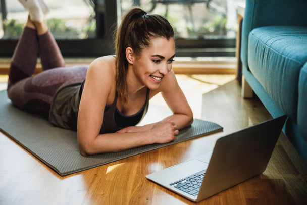 Молода жінка використовує ноутбук під час виконання розтяжок вдома вранці
. - Фото, зображення